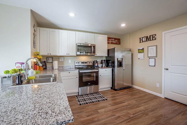 A modern kitchen with white cabinets, stainless steel appliances, and a wooden floor.