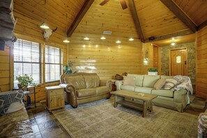 A log cabin interior with a leather sofa, a wooden coffee table, and a stone wall. - 2 Mi to Historic Dtwn! Family Getaway w/ Game Room (Granbury)