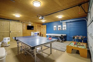 Een kamer met een tafeltennistafel, een wasmachine, een tafelvoetbaltafel en een kleine speelhoek.