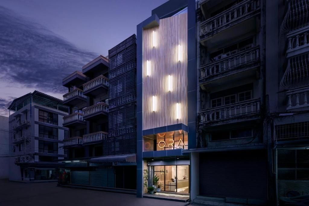 Un edificio moderno con un llamativo letrero 'ORA', varios balcones y un escaparate de vidrio.
