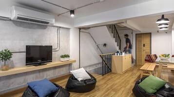 Un espacio moderno para vivir con televisión de pantalla plana, pufs, una escalera y una pequeña cocina.