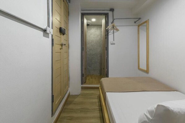 Una habitación estrecha con una cama, un armario y una puerta que da a otra habitación.