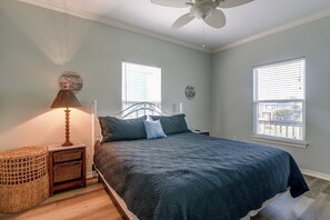 Ein Schlafzimmer mit einem Bett, einem Nachttisch, einer Lampe, einer Wanduhr und zwei Fenstern mit Jalousien.