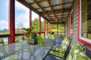 A covered outdoor seating area with metal tables and chairs, surrounded by glass walls and a wooden ceiling. - On 62-Acre Farm! Waterfront Home w/ Decks & Views (Meadows of Dan)