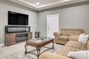 A living room with a flat-screen TV, a wooden cabinet, a glass coffee table, a patterned sofa, and a door. - San Benito Home w/ Pool, Close to Dtwn (San Benito)