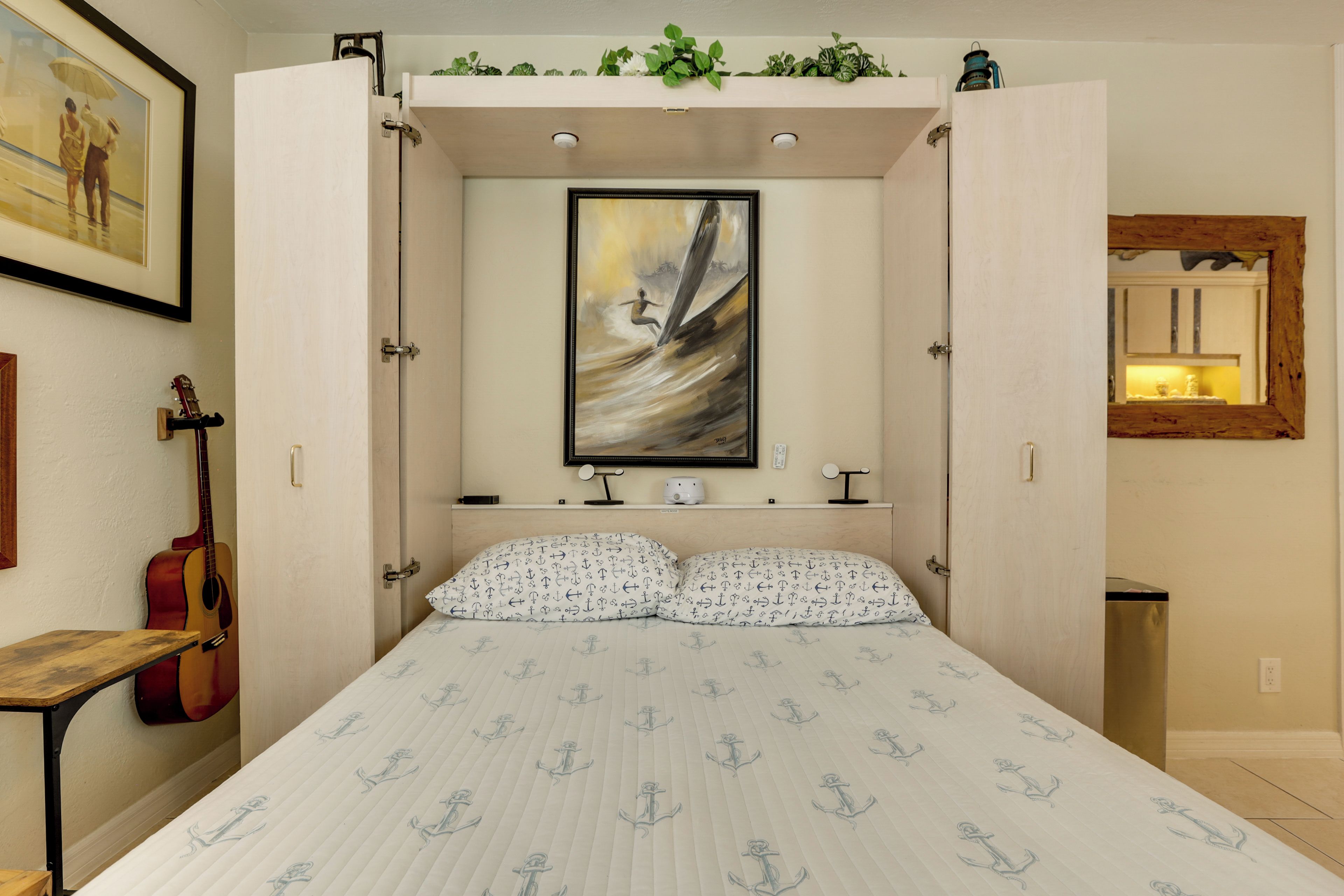 Een slaapkamer met een bed, een gitaar, een lijst met een schilderij en een spiegel.