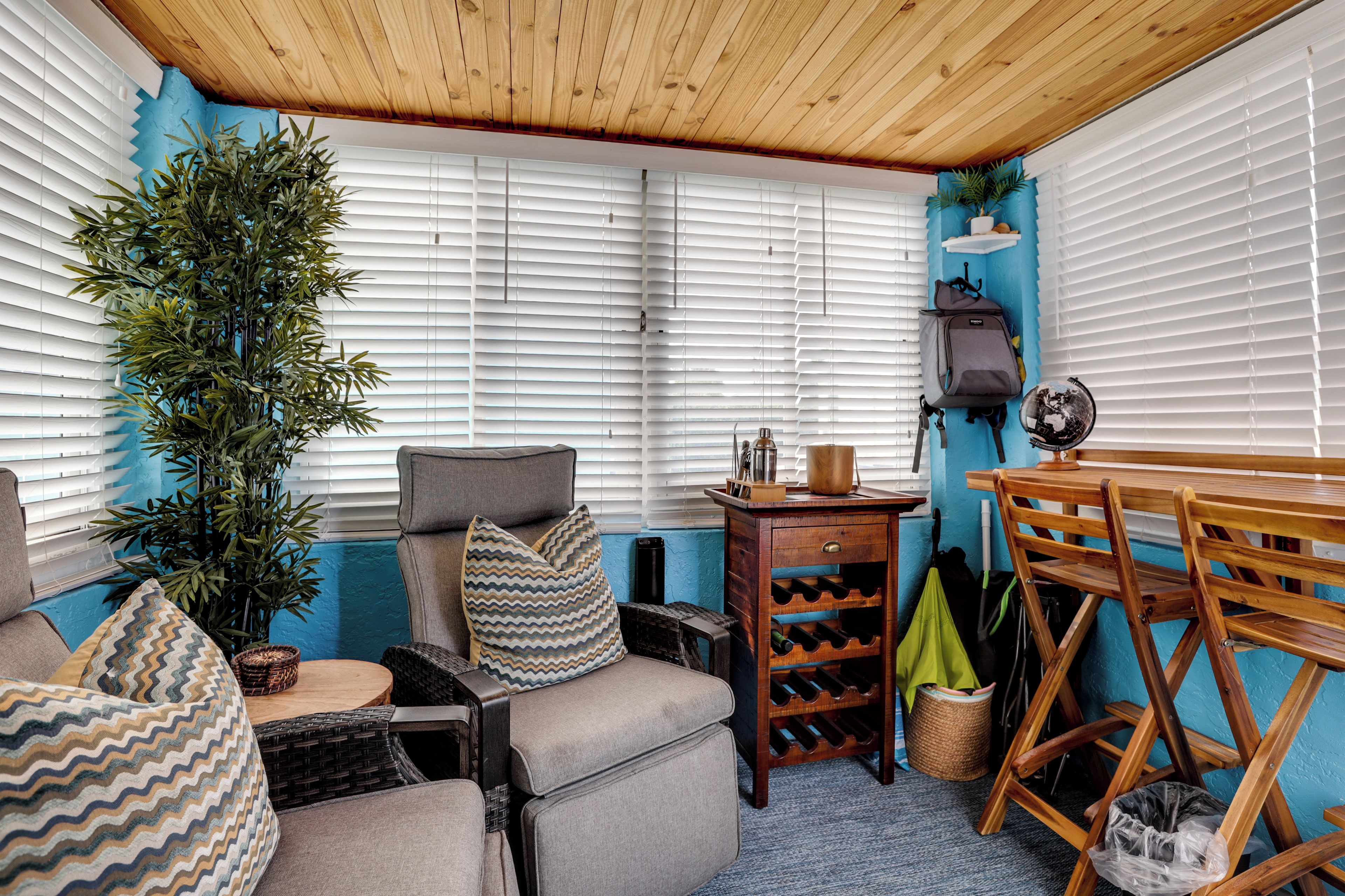 Een knus vertrek met een houten plafond, een bank met gestreepte kussens, een kleine tafel en een wijnrek.
