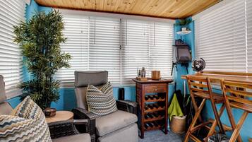 Een knus vertrek met een houten plafond, een bank met gestreepte kussens, een kleine tafel en een wijnrek.