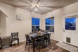 A dining area with a table set for six, surrounded by chairs, with a view of the outside through large windows. - 7 Mi to SeaWorld! Group-Friendly Getaway w/ Pool (San Antonio)