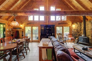 A spacious cabin interior with a high ceiling, wooden walls, a stone fireplace, and a dining area with a long table and chairs. - Dock & River Access: Custom-Built Cabin in Oneonta (Oneonta)