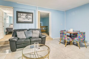 A living room with a black leather sofa, a glass coffee table, and a dining table with floral chairs.