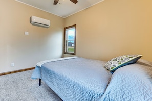 A bedroom with a bed, a window, an air conditioning unit, and a ceiling fan.