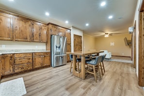 A kitchen with wooden cabinets, a stainless steel refrigerator, and a dining area with a wooden table and chairs.