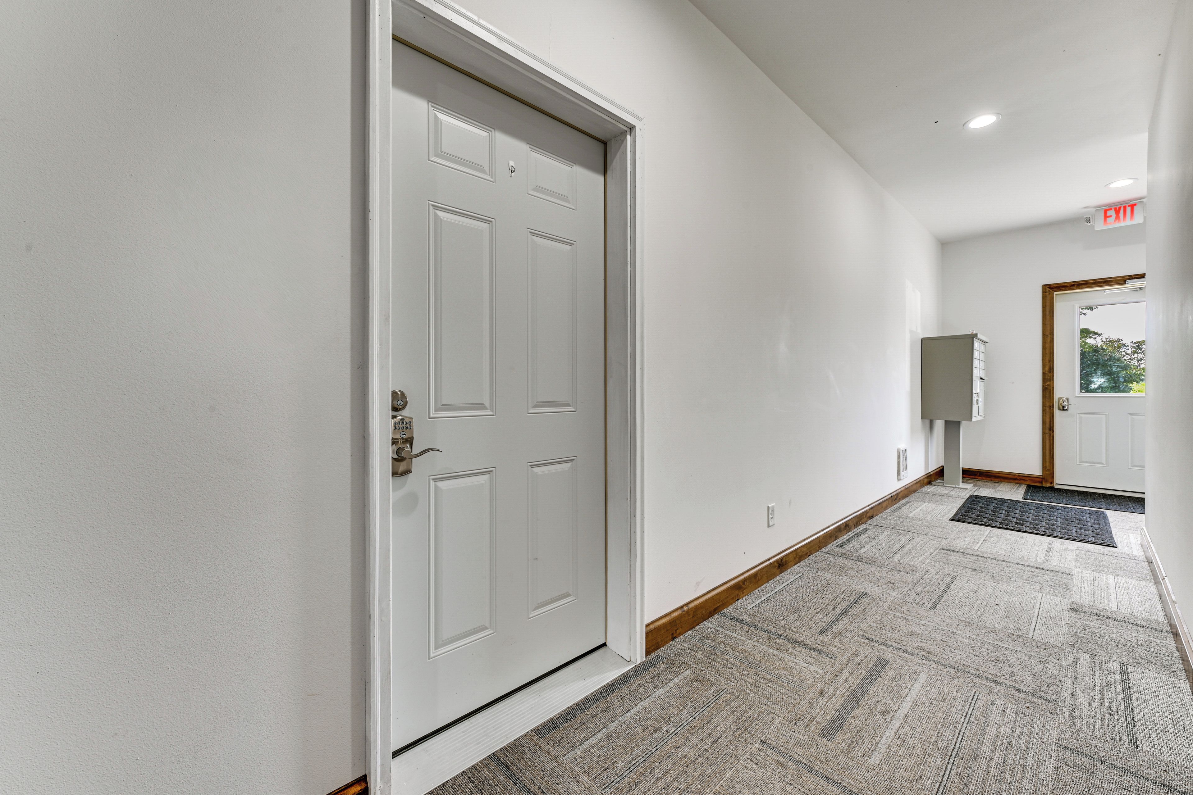 A hallway with a white door, a mailbox, and a doormat.