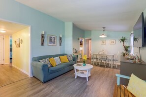 A living room with a sofa, a dining table with chairs, and a kitchen area in the background. - Gaston Lake House: Dock, Deck, Game Room! (Bracey)
