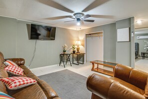 A living room with a ceiling fan, a flat-screen TV mounted on the wall, a coffee table, and a sofa with patterned cushions. - Central Rio Grande Valley Hub w/ Full Kitchen! (La Feria)