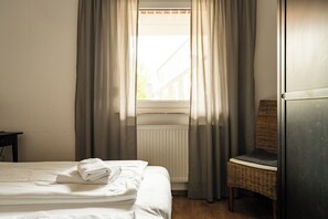 A hotel room with a bed, a chair, a radiator, and a window with curtains. - A gorgeous vacation apartment with a sauna and fireplace near the beach in Röbel Müritz (Röbel/ Müritz)