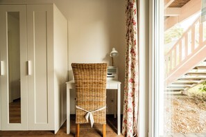 A wicker chair with a white cushion tied with a ribbon, a desk with a lamp, and a window with floral curtains. - A gorgeous vacation apartment with a sauna and fireplace near the beach in Röbel Müritz (Röbel/ Müritz)