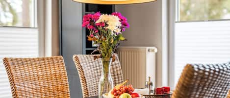 A dining table with a vase of flowers, a fruit basket, and a candle holder.
