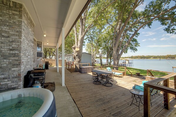 Eine überdachte Terrasse mit Whirlpool, Gartenmöbeln und Seeblick.