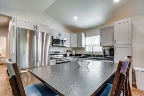 A modern kitchen with stainless steel appliances, a granite countertop, and a dining area with a glass bowl centerpiece. - *New To Market* | Riverfront Pigeon Forge Retreat (Pigeon Forge)