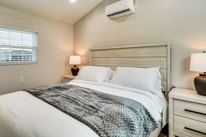 A bedroom with a bed, bedside tables, a lamp, an air conditioner, and a window with blinds. - *New To Market* | Riverfront Pigeon Forge Retreat (Pigeon Forge)