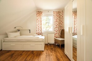 A bedroom with a bed, a chair, a wardrobe, and a window with curtains. - Cozy vacation apartment with a sauna in Röbel on Lake Müritz (Röbel)