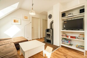 A cozy living room with a sofa, a small table, a fireplace, and a bookshelf filled with books and games. - Cozy vacation apartment with a sauna in Röbel on Lake Müritz (Röbel)