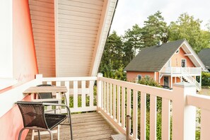 A wooden deck with a table and a chair, a white railing, and a view of houses in the background. - Cozy vacation apartment with a sauna in Röbel on Lake Müritz (Röbel)
