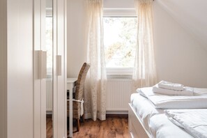 A bedroom with a bed, a chair, a window with curtains, and a radiator. - Cozy vacation apartment with a sauna in Röbel on Lake Müritz (Röbel)