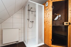 A shower area with a glass door, a wooden sauna door, and a white radiator. - Cozy vacation apartment with a sauna in Röbel on Lake Müritz (Röbel)