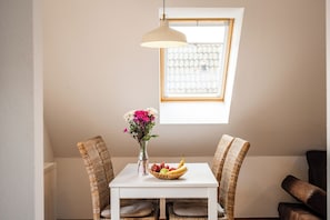 A dining area with a table, chairs, a vase with flowers, and a basket of fruit. - Cozy vacation apartment with a sauna in Röbel on Lake Müritz (Röbel)