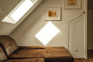 A room with a sloped ceiling, a brown sofa, and two framed pictures on the wall. - Cozy vacation apartment with a sauna in Röbel on Lake Müritz (Röbel)