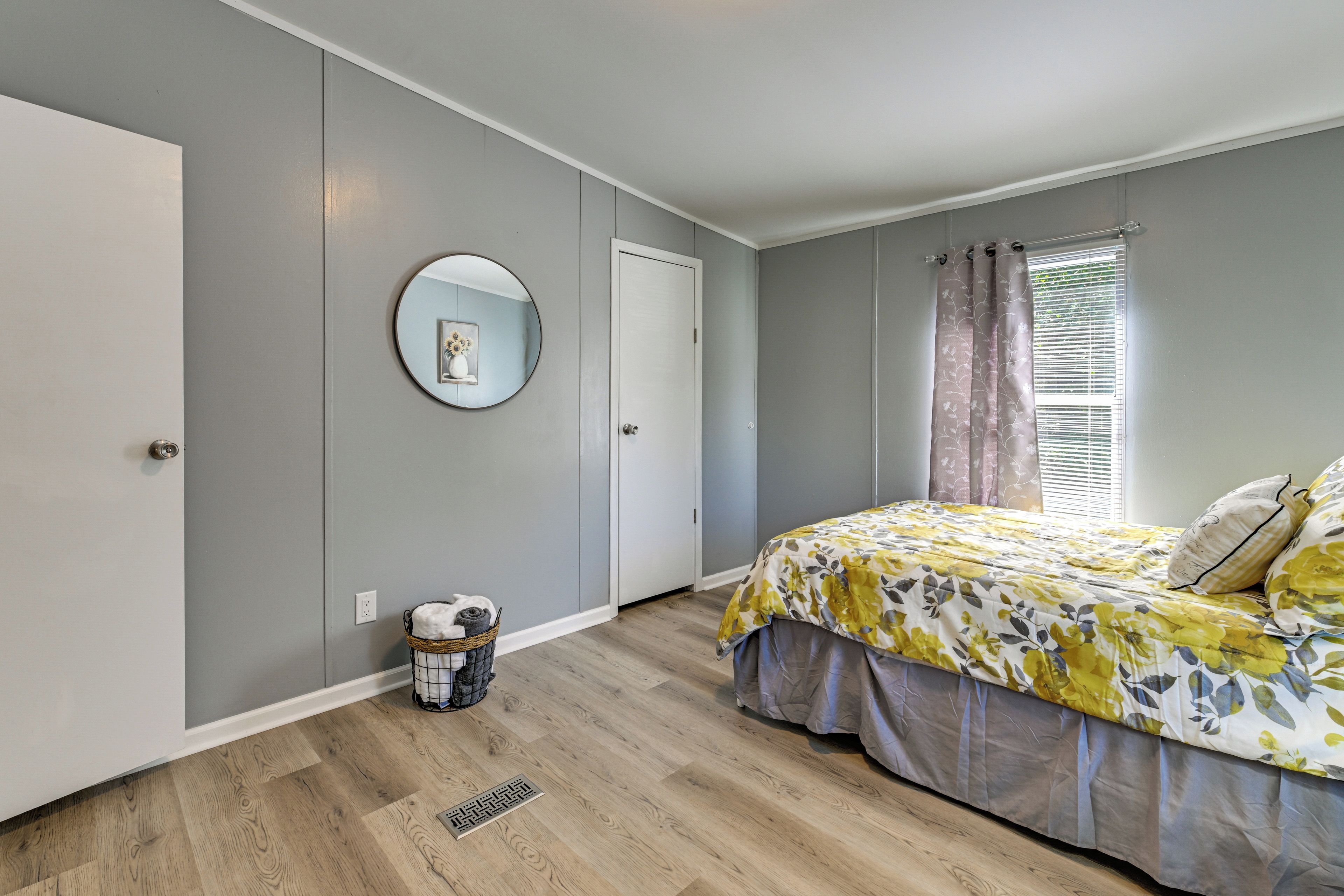 Een slaapkamer met een bed, een ronde spiegel, een deur en een raam met gordijnen.