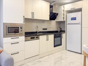A modern kitchen with white cabinets, a built-in oven, a microwave, and a refrigerator. - Qoople Elize A17 - Cozy 1-bedroom apartment in Alanya (Alanya)