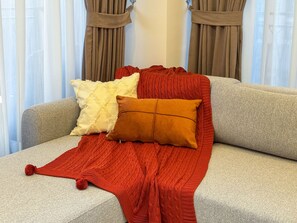 Un sofá con un plaid rojo de punto, dos almohadas y una ventana con cortinas.