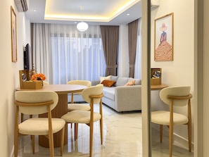 Una sala de estar moderna con comedor, que incluye un sofá, una mesa de centro y un televisor montado en la pared.