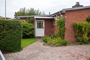 Ein Ziegelhaus mit weißer Tür, umgeben von einem gepflegten Garten und einem gepflasterten Auffahrt.