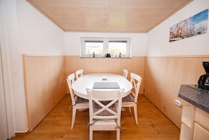Ein Zimmer mit einem runden Tisch, weißen Stühlen, einem Fenster mit Aussicht und einem Gemälde an der Wand.