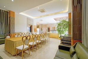 Un salón de conferencias con una larga mesa y sillas, un sofá, una planta en maceta y una escalera.