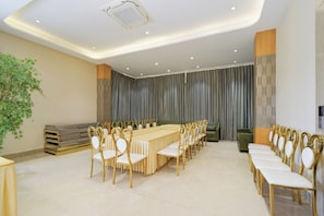 A conference room with a long table and chairs, a plant, and a grey curtain backdrop.