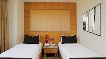 A hotel room with two beds, a wooden headboard, a nightstand with a phone, and a painting on the wall.