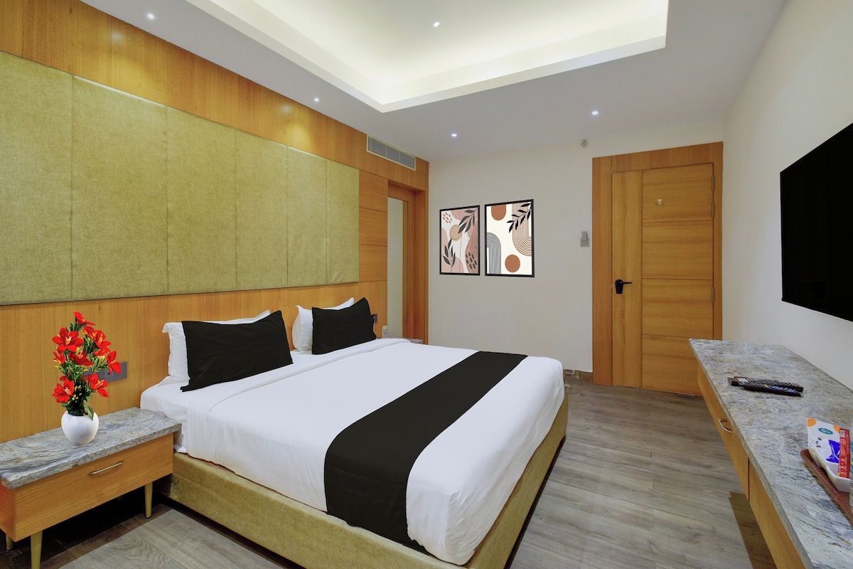 Habitación de hotel con cama, mesitas de noche, escritorio, televisor y obras de arte en las paredes.