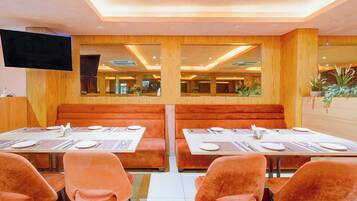A restaurant with booths and tables, a flat-screen TV mounted on the wall, and potted plants on the side.