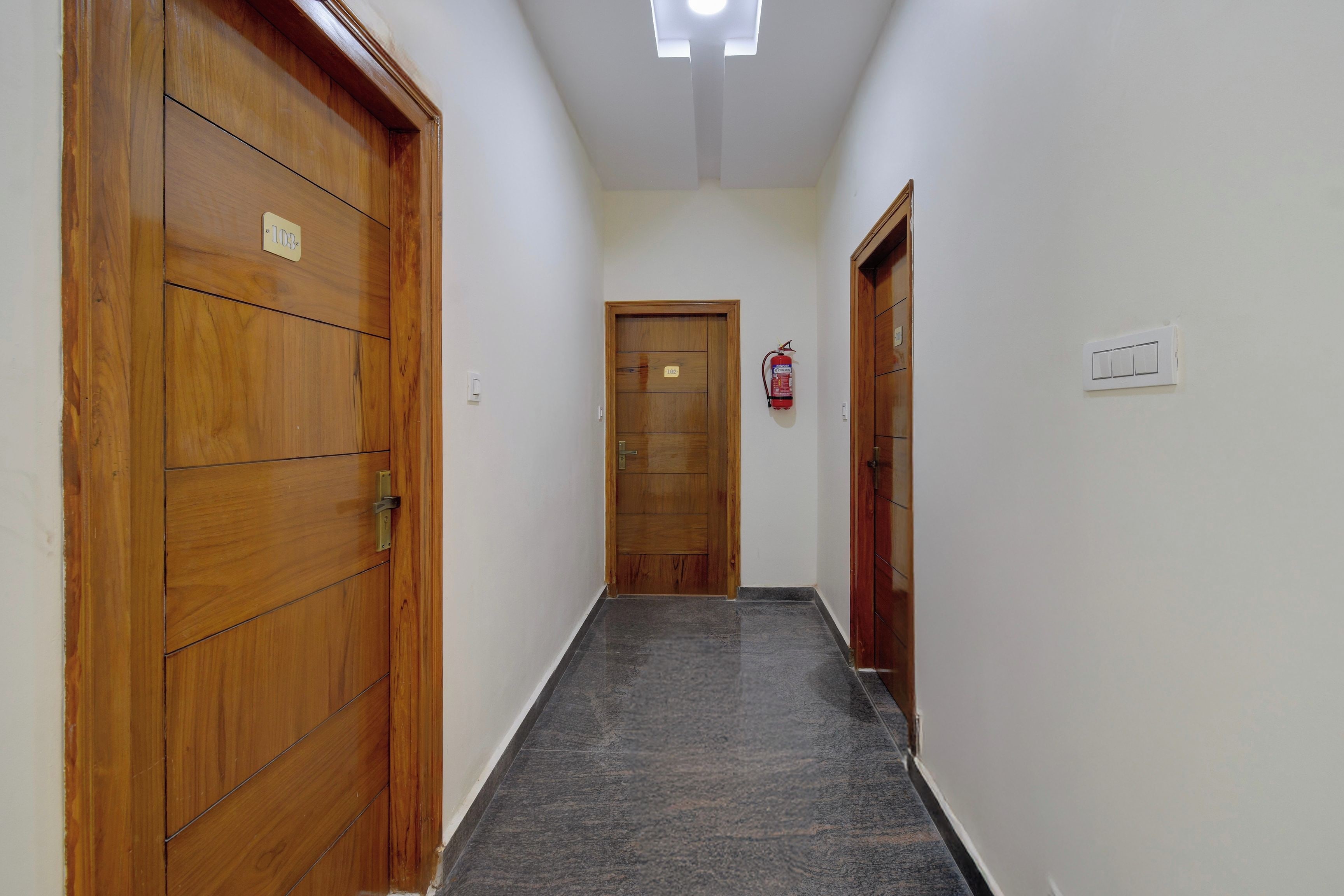 Un pasillo con puertas de madera, un extintor y un interruptor de luz en la pared.
