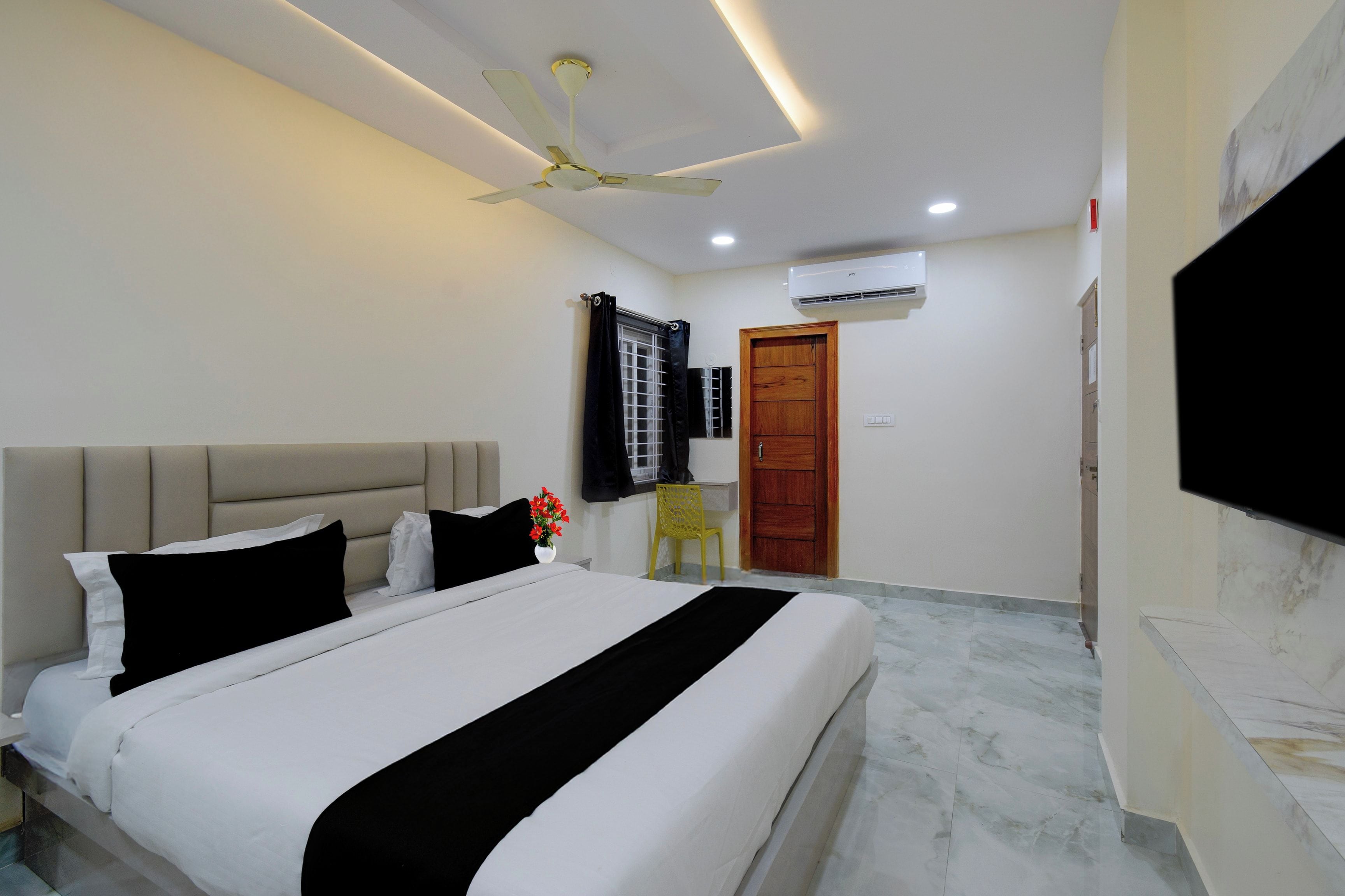 A hotel room with a bed, a ceiling fan, an air conditioning unit, a TV, and a wooden door.