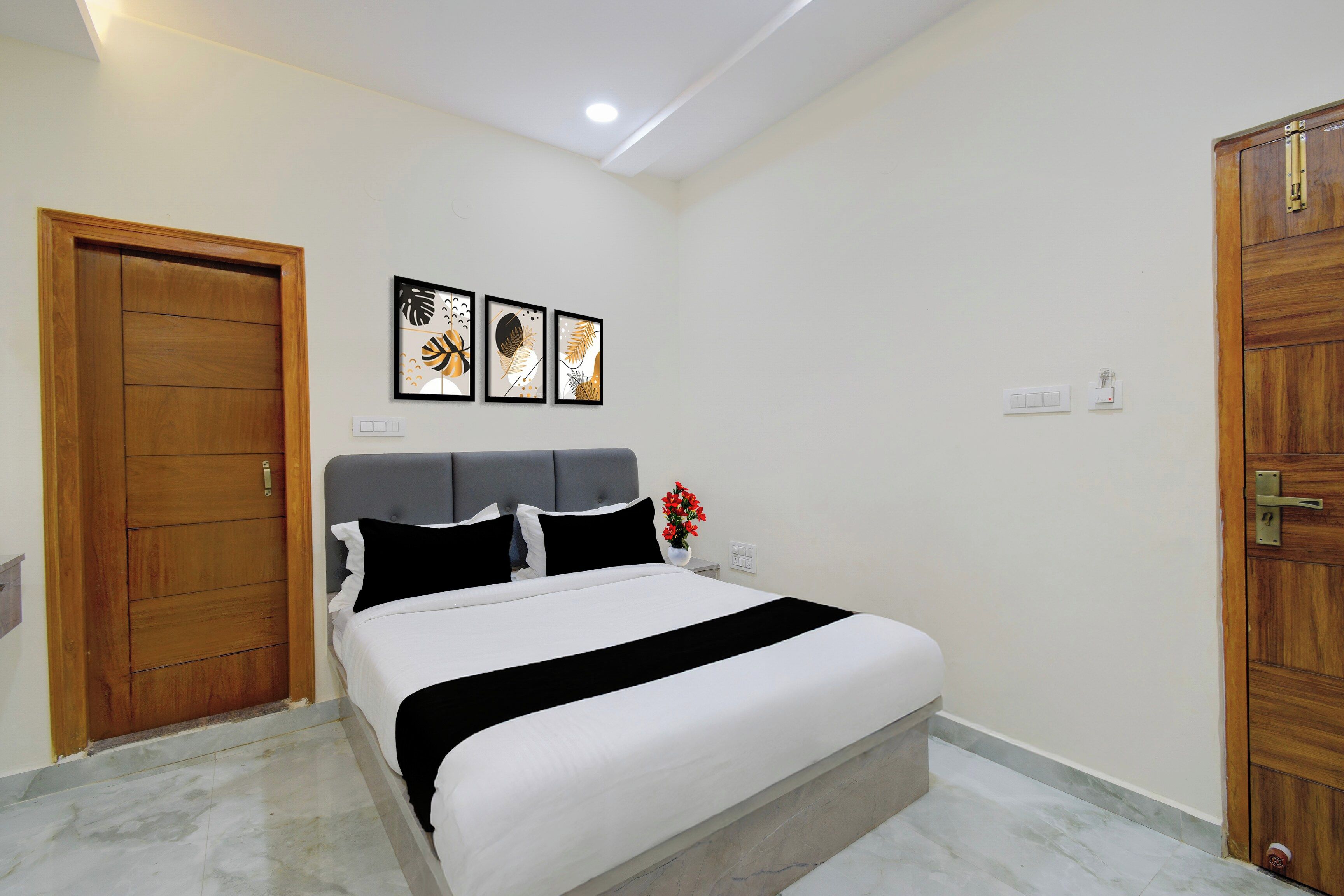 Un dormitorio con cama, puerta de madera, lámpara de pared y tres cuadros enmarcados.