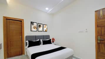 Un dormitorio con cama, puerta de madera, lámpara de pared y tres cuadros enmarcados.