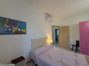 Ein Schlafzimmer mit Bett, Nachttischlampe, Spiegel, Kleiderschrank und einem Bild an der Wand.