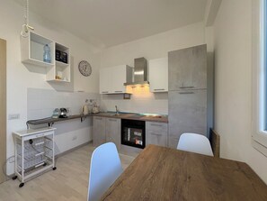 A modern kitchen with white cabinets, a stainless steel range hood, a built-in oven, and a dining table with chairs. - Beautiful  villa with private pool, A/C, WIFI, TV, patio, pets allowed and panoramic view (Marina Di Ragusa)